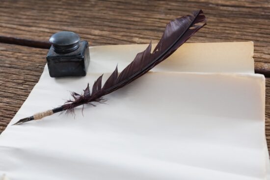 Quill pen and ink bottle beside blank parchment