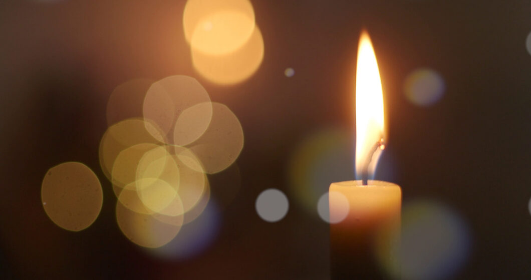 Single candle flame glowing in deep darkness