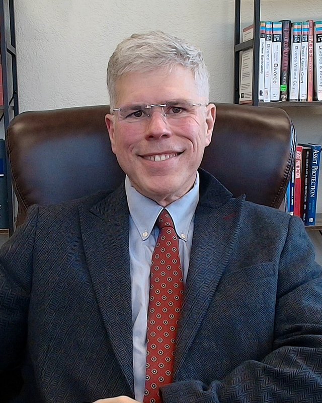 Edward J. Barton in a dark tweed jacket and red tie, seated in his law office